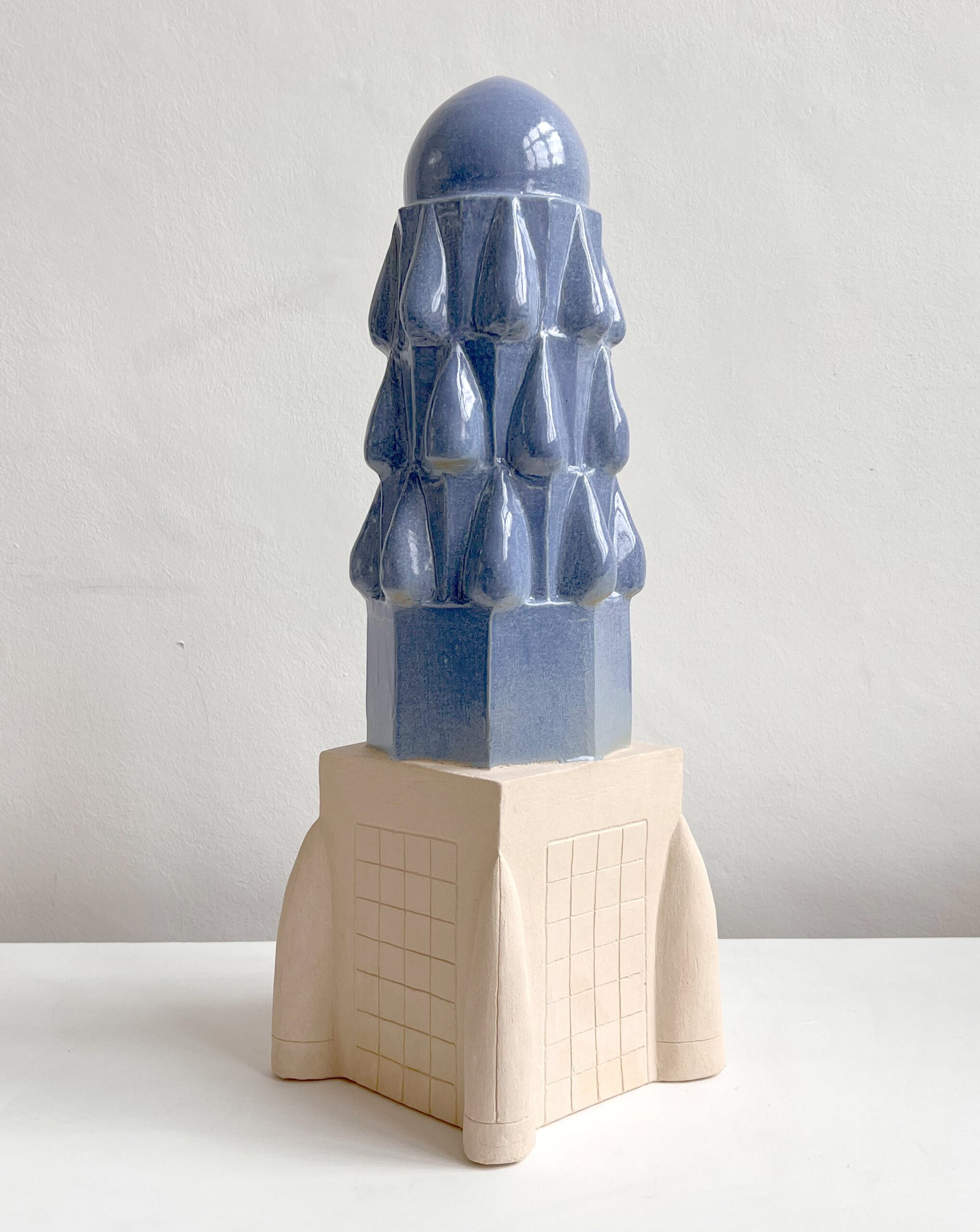 Blue dome-shaped sculpture with rounded top and water-droplet shaped designs on the side mounted on a being base