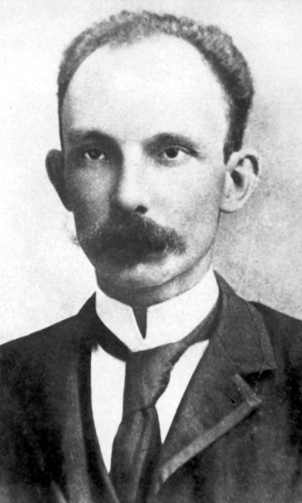 Thin man with large curved mustache wearing a high collared white shirt with tie and jacket