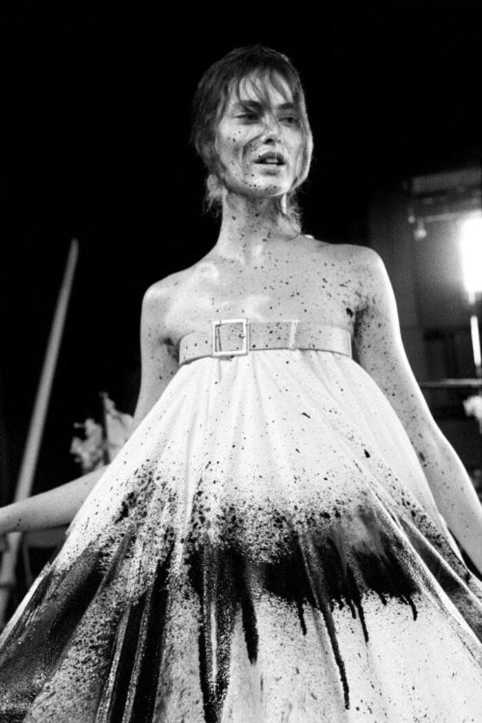 Black and white photo of woman walking a runway splattered with black paint