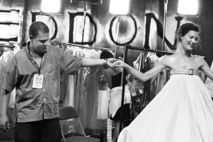 Photo of Alexander McQueen holding a model's hand wearing a white gown as they both smile.