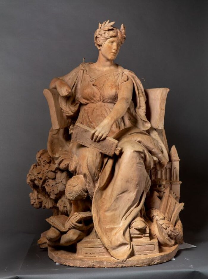 Sculpture of a woman sitting on a large chair draped in a gown with a small child curled up on the ground below her reading a book