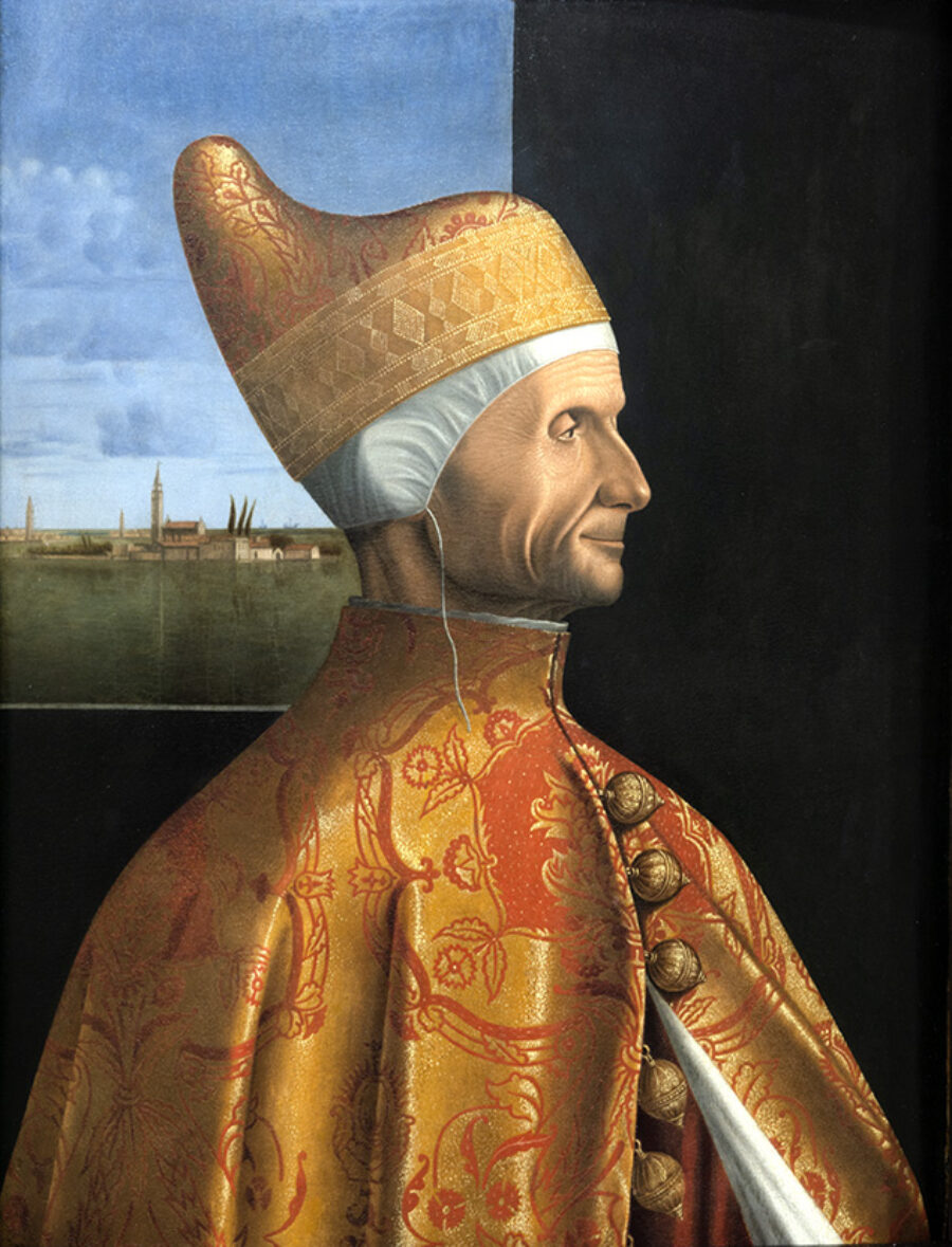 Man posed looking to the side waring an intricate gold robe with large round gold buttons and matching gold hat.