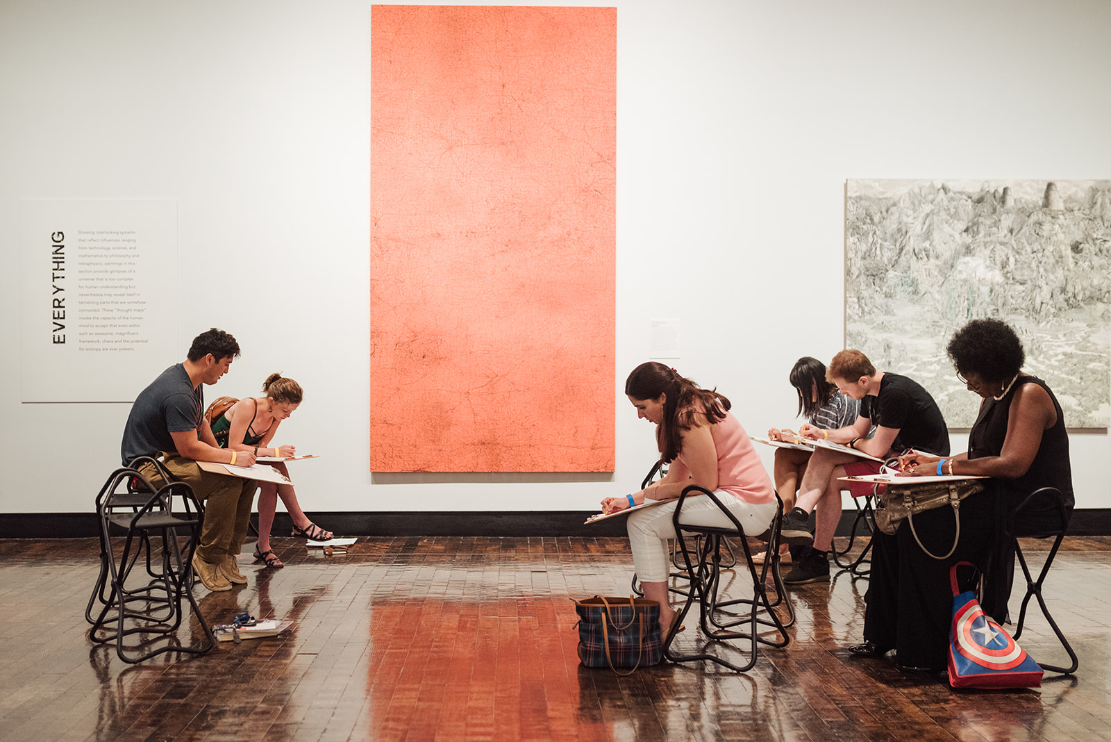 Guests sitting on stools in the gallery writing on a pad.