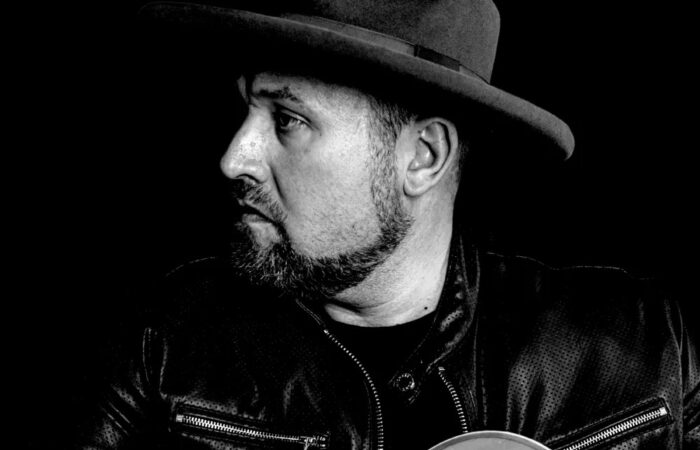 Musician Ronny Criss hold a guitar in a black and white photo.