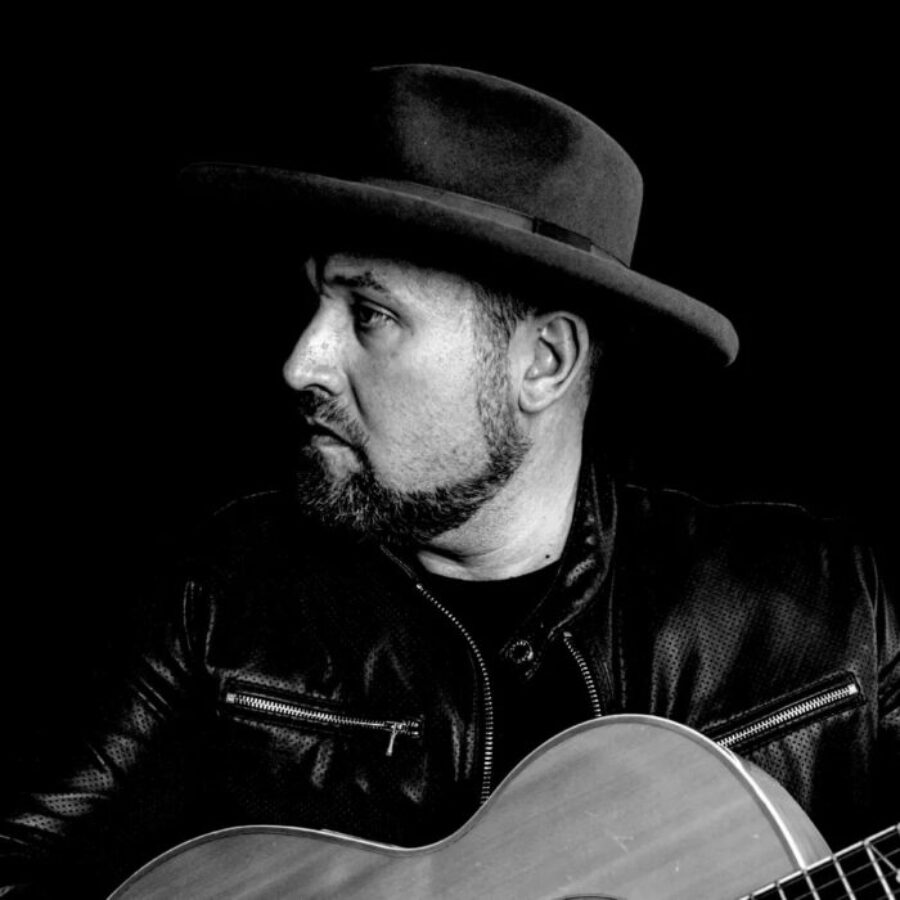 Musician Ronny Criss hold a guitar in a black and white photo.