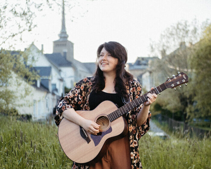 Singer Claire Kelly holds a guitar in a field