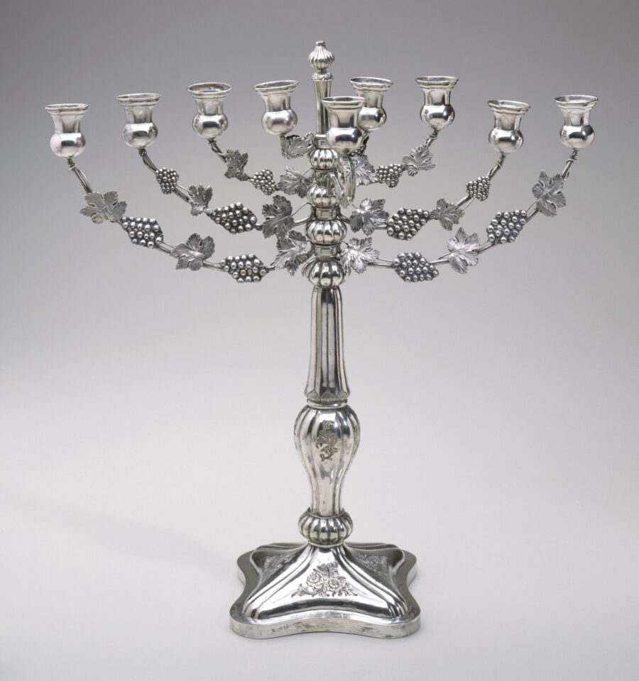A silver Menorah with etched grapes and leaves.