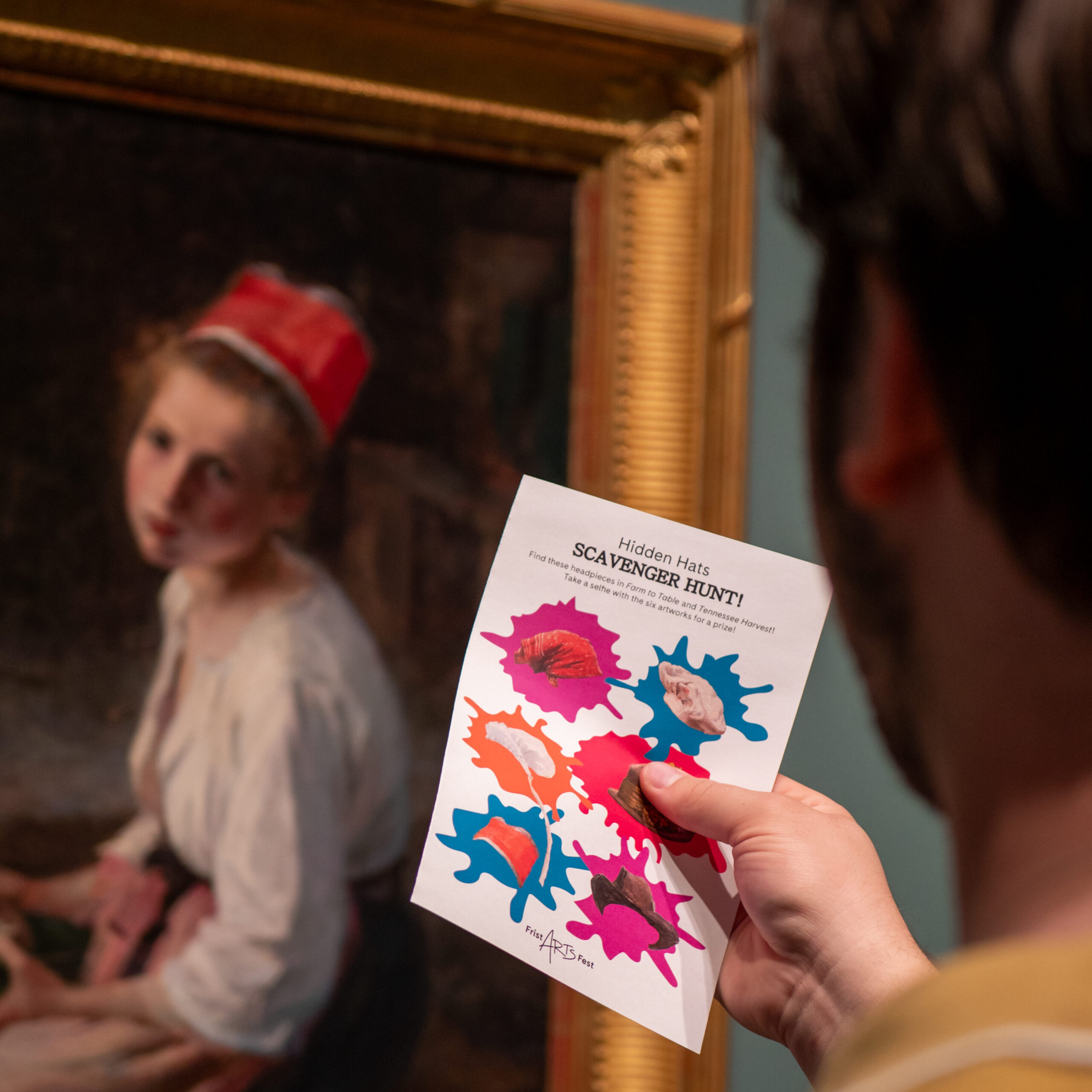Man holds up scavenger hunt card in front of a painting.