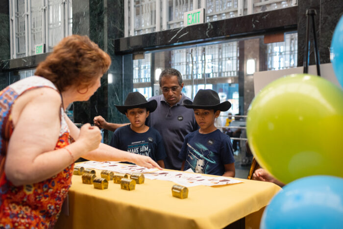 Father and two sons wearing cowboy hats watching a woman demonstrating an activity