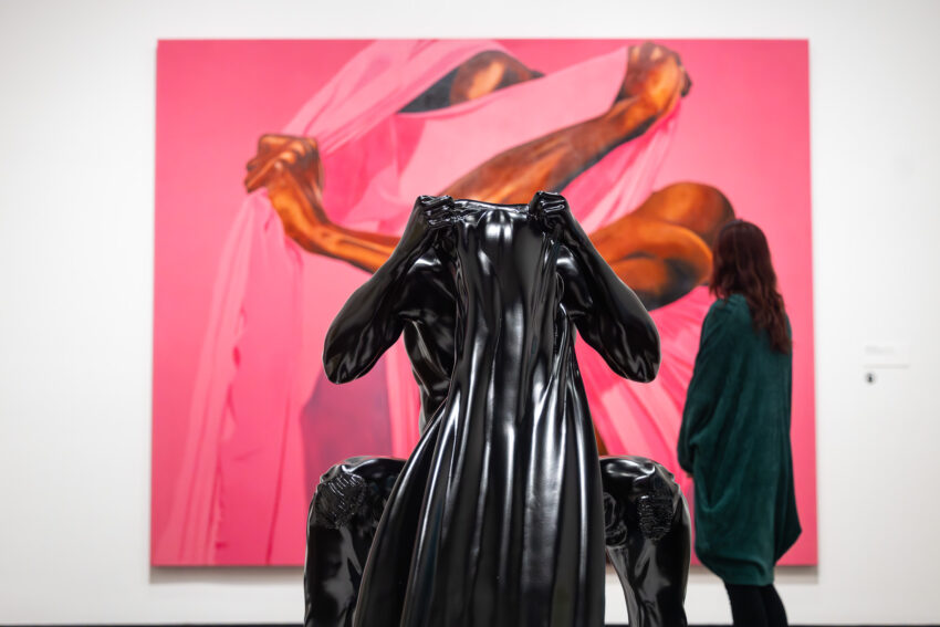 Woman views a pink painting by Fahamu Pecou.
