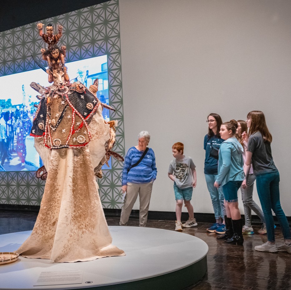 Family standing together looking curiously at a display of a masquerade