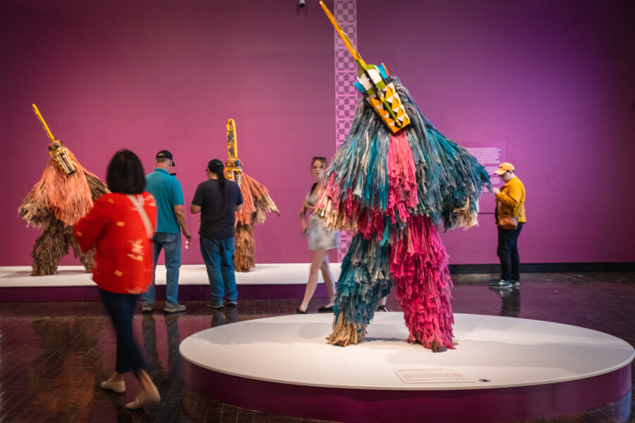 Bright colored African Masquerade with people walking around it.