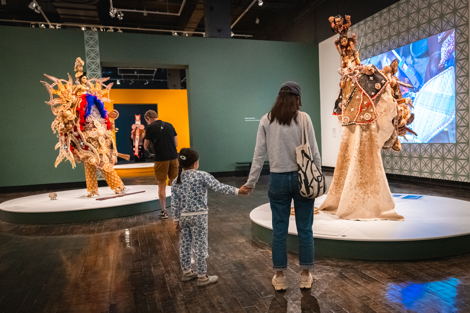 Mom holding her daughters hand looking at large masquerade ensembles