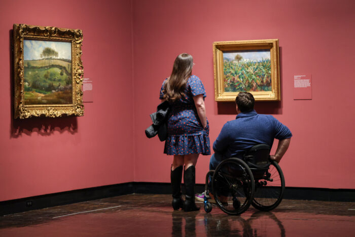 Couple looking at a painting in the gallery. The man is in a wheelchair.