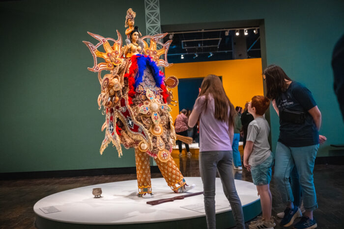 Three people look at an African Masquerade in an art museum.