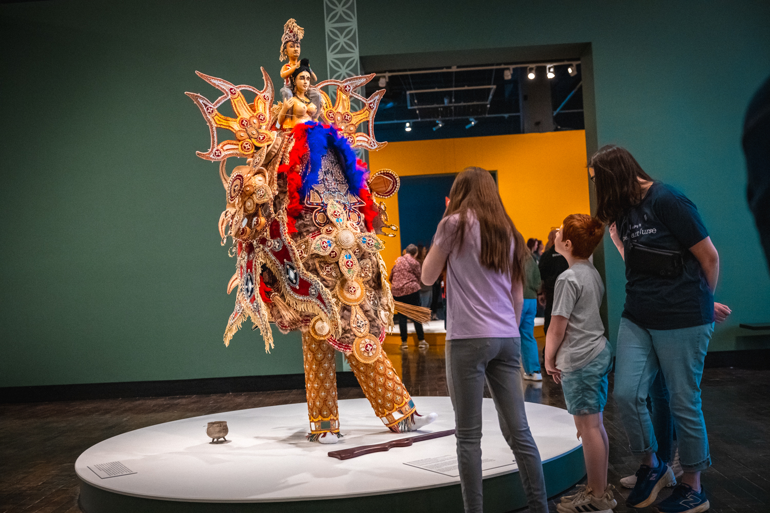 Three people look at an African Masquerade in an art museum.