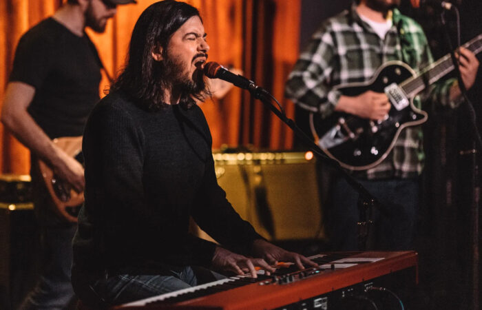 A man plays piano and sings with a band behind him.