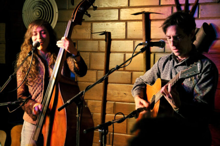 A woman plays the cello and a man plays the guitar on a stage.