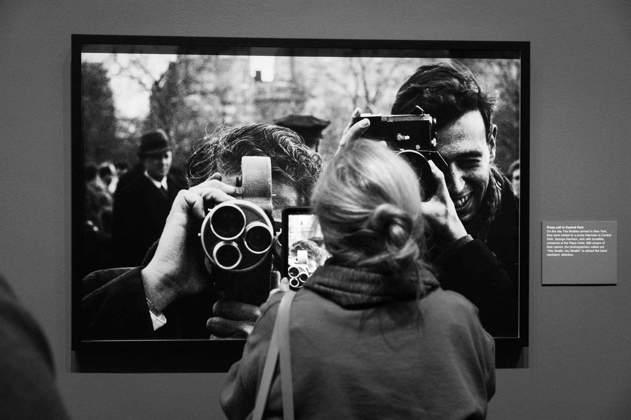 Woman taking a photo with her phone of a photograph of two men with cameras.
