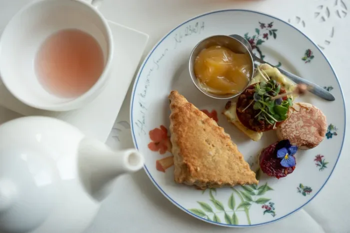 A place setting with a teapot and a plate with a variety of small bites on it.