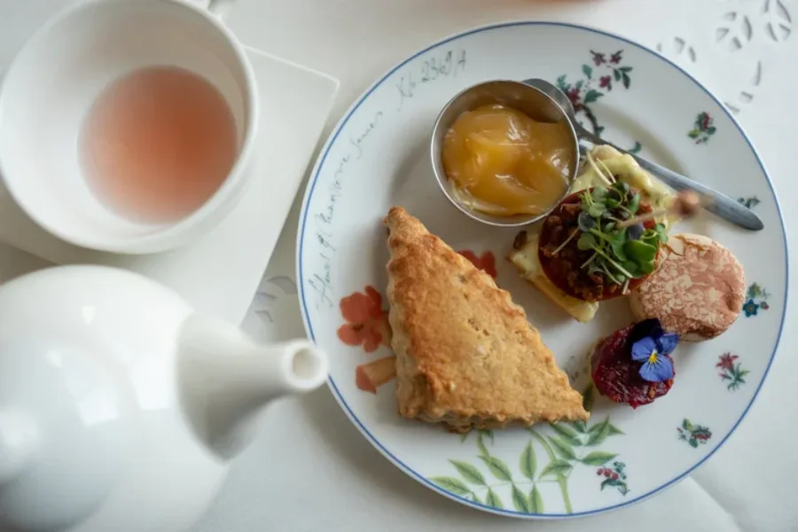 A place setting with a teapot and a plate with a variety of small bites on it.