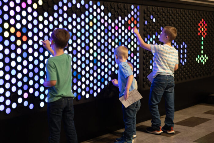 Three young children play with a light bright wall.