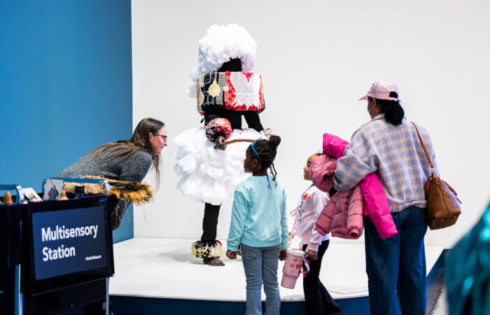 Two young girls look at a sensory cart in an art museum with two adults.