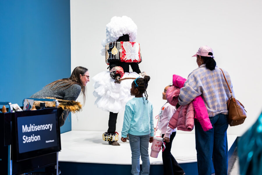 Two young girls look at a sensory cart in an art museum with two adults.