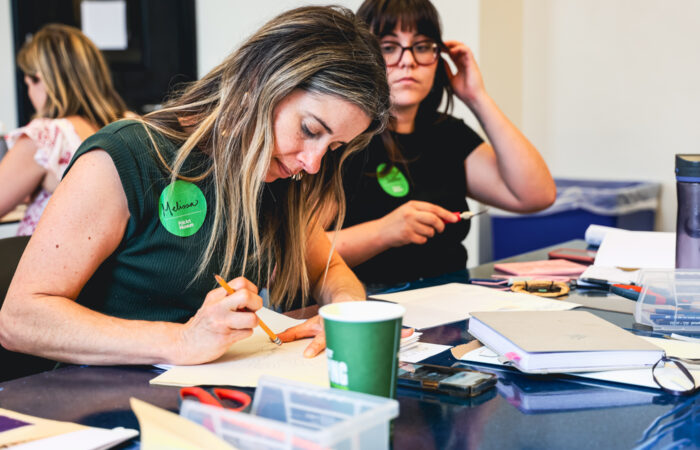 A woman sketches on a piece of paper in an art class.