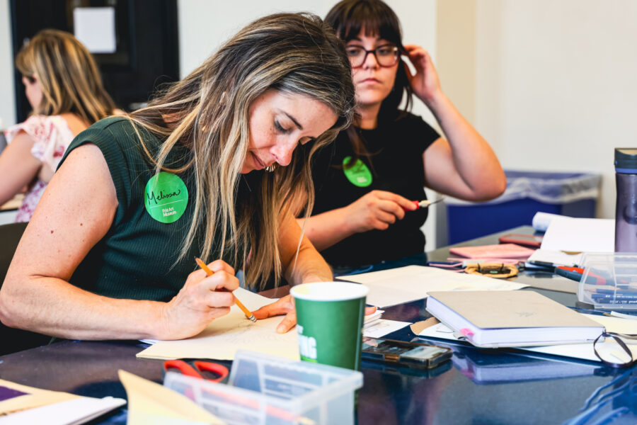 A woman sketches on a piece of paper in an art class.
