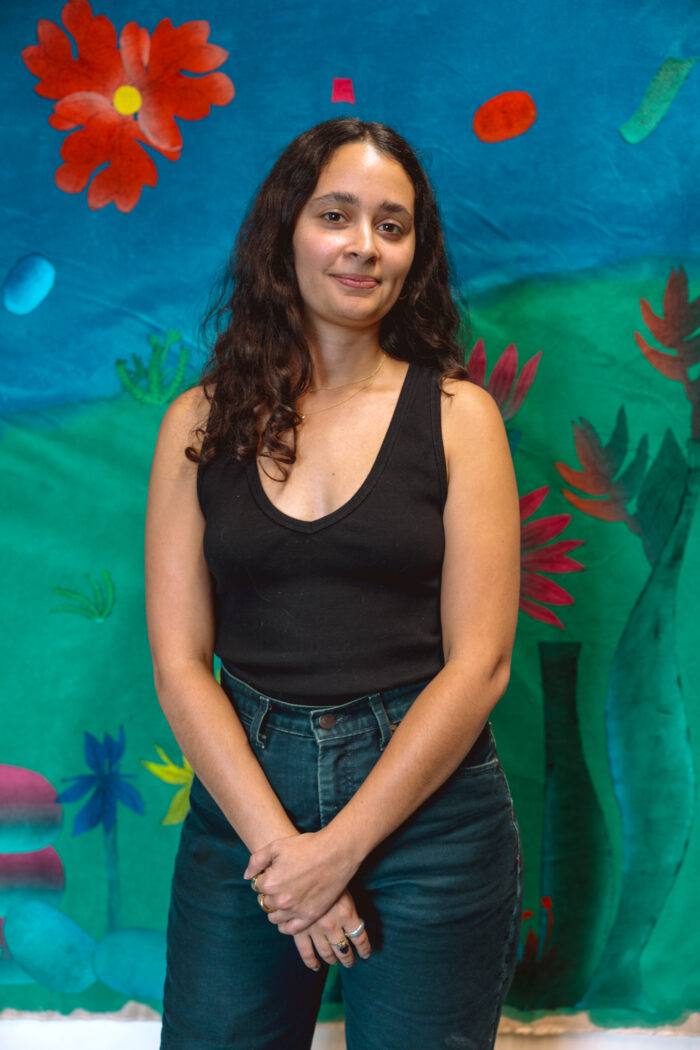 Headshot of artist Yanira Vissepo in front of one of her pieces. 