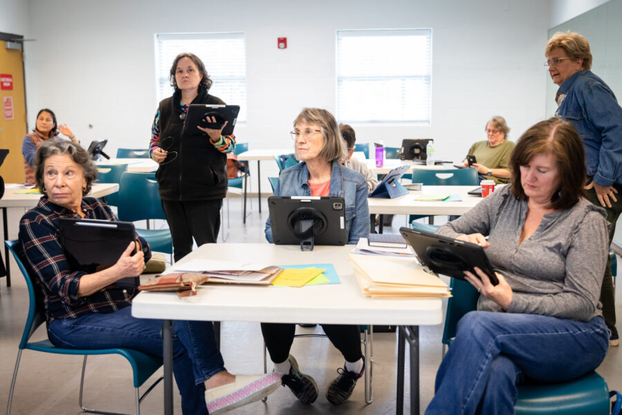 A group of adults look at iPads in a class.