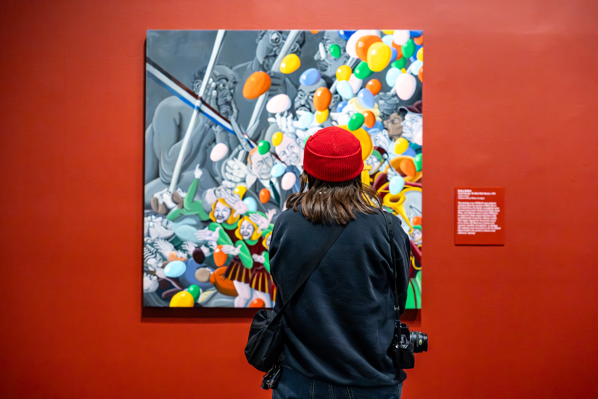 Woman in a red hat looking at a colorful painting hung on a red wall