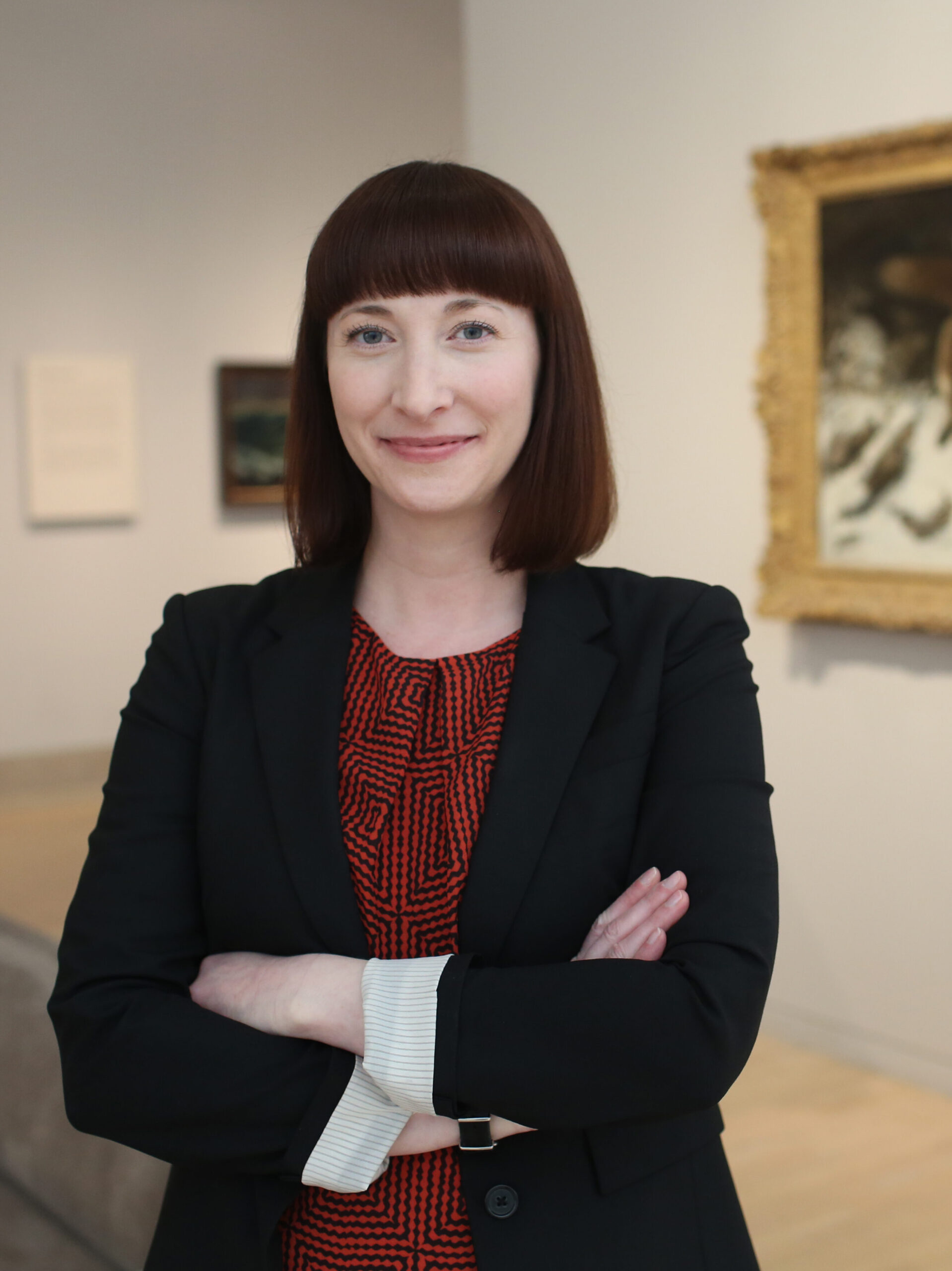 A woman with short dark hair poses in an art gallery.
