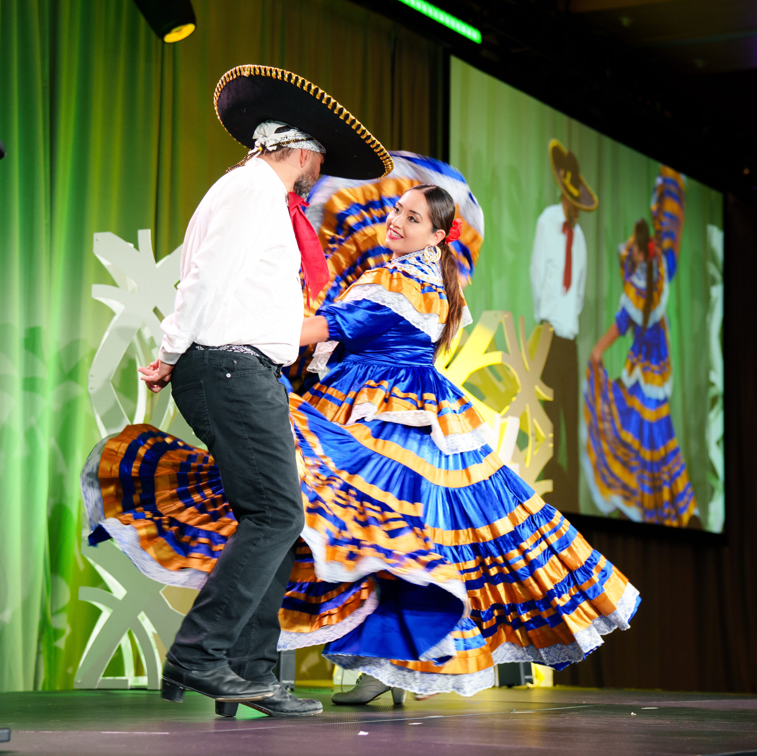 A man and woman dance together in traditional Mexican costumes. 