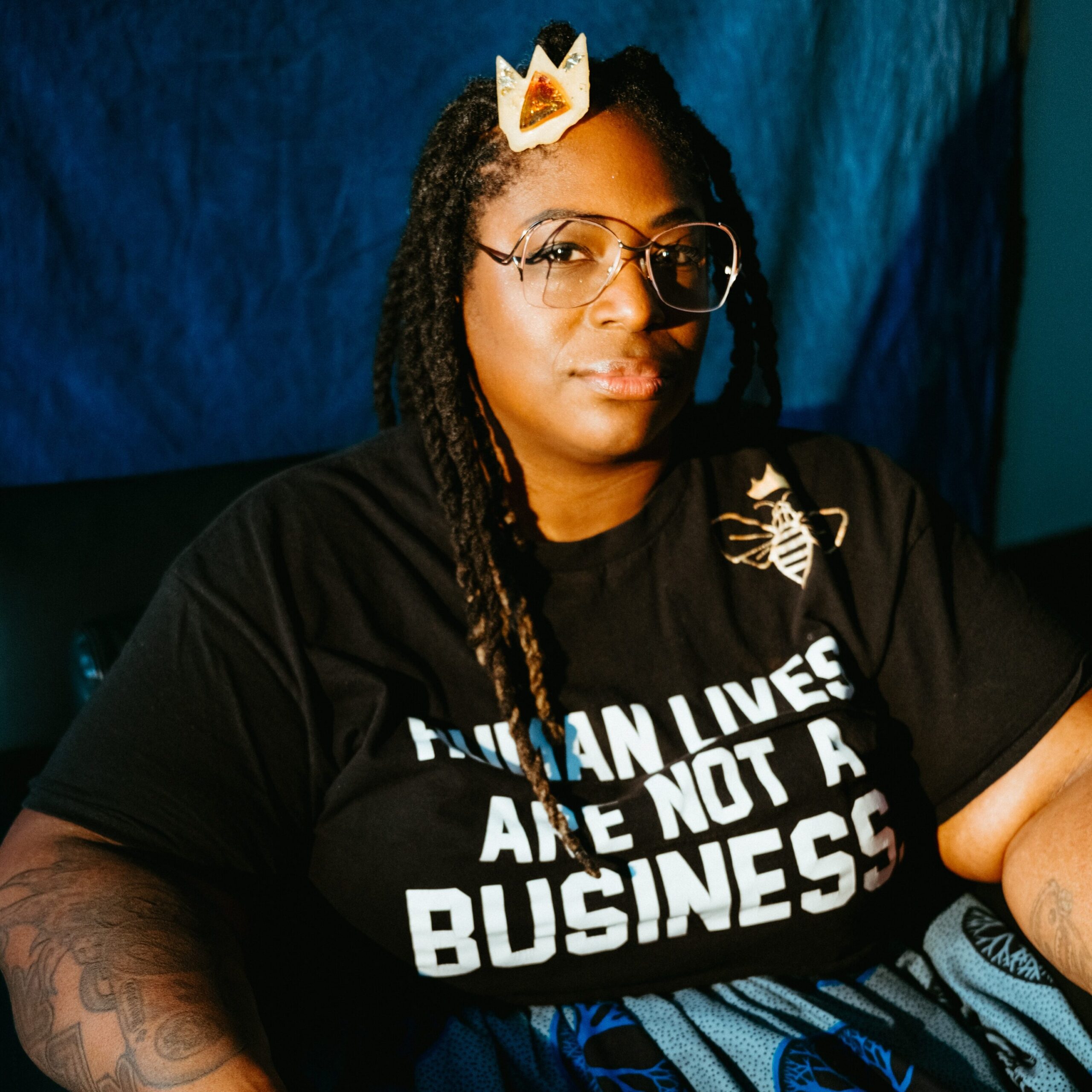 Artist Elisheba Israel Mrozik poses in front of a blue background with a crown clip in her hair.