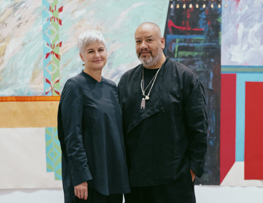 A man and woman stand together in front of an abstract artwork.