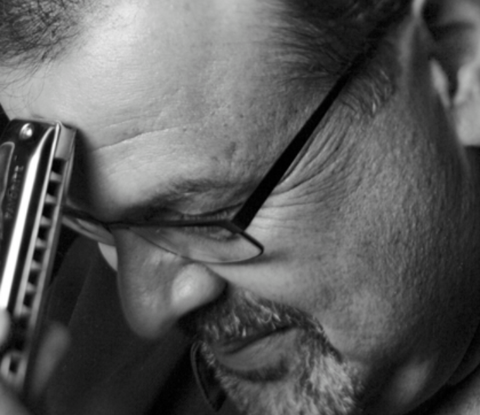 A black and white image of a man's face with a harmonica touching his forehead.