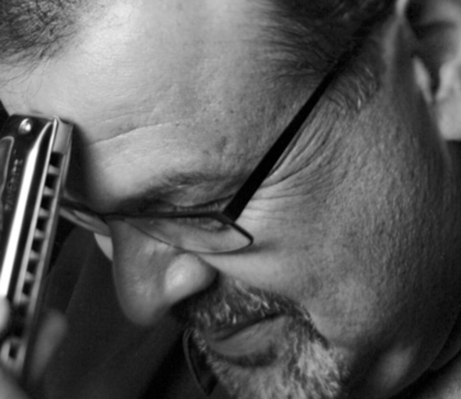 A black and white image of a man's face with a harmonica touching his forehead.