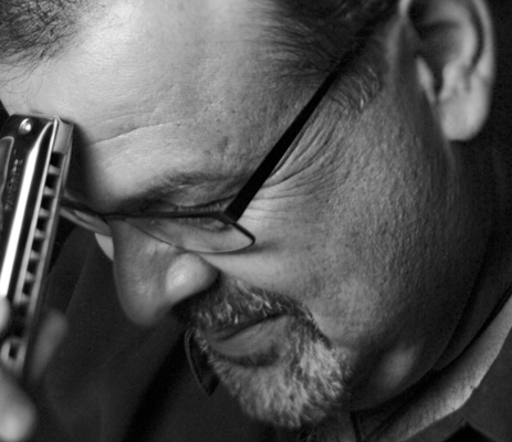 A black and white image of a man's face with a harmonica touching his forehead.