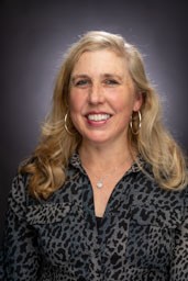 A blonde woman in a leopard shirt poses for a head shot.
