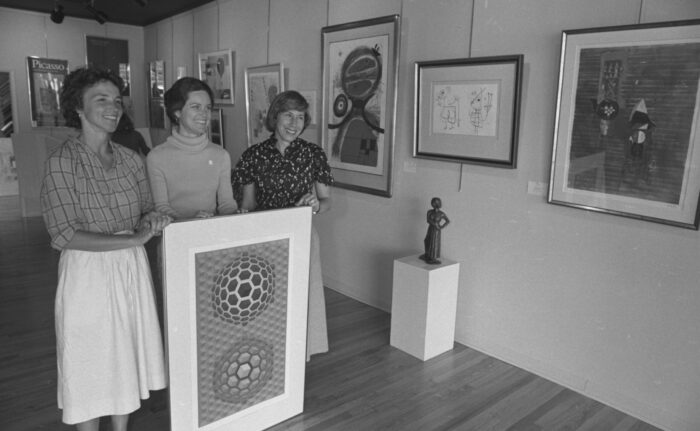 Three women pose with an art piece in an old black and white photo.