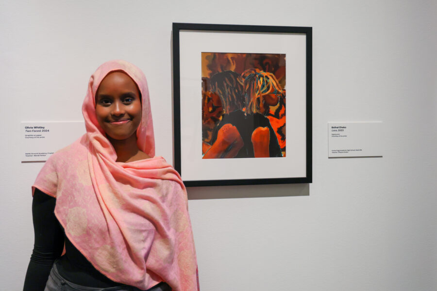 Young woman standing in front of her painting in a student art show.