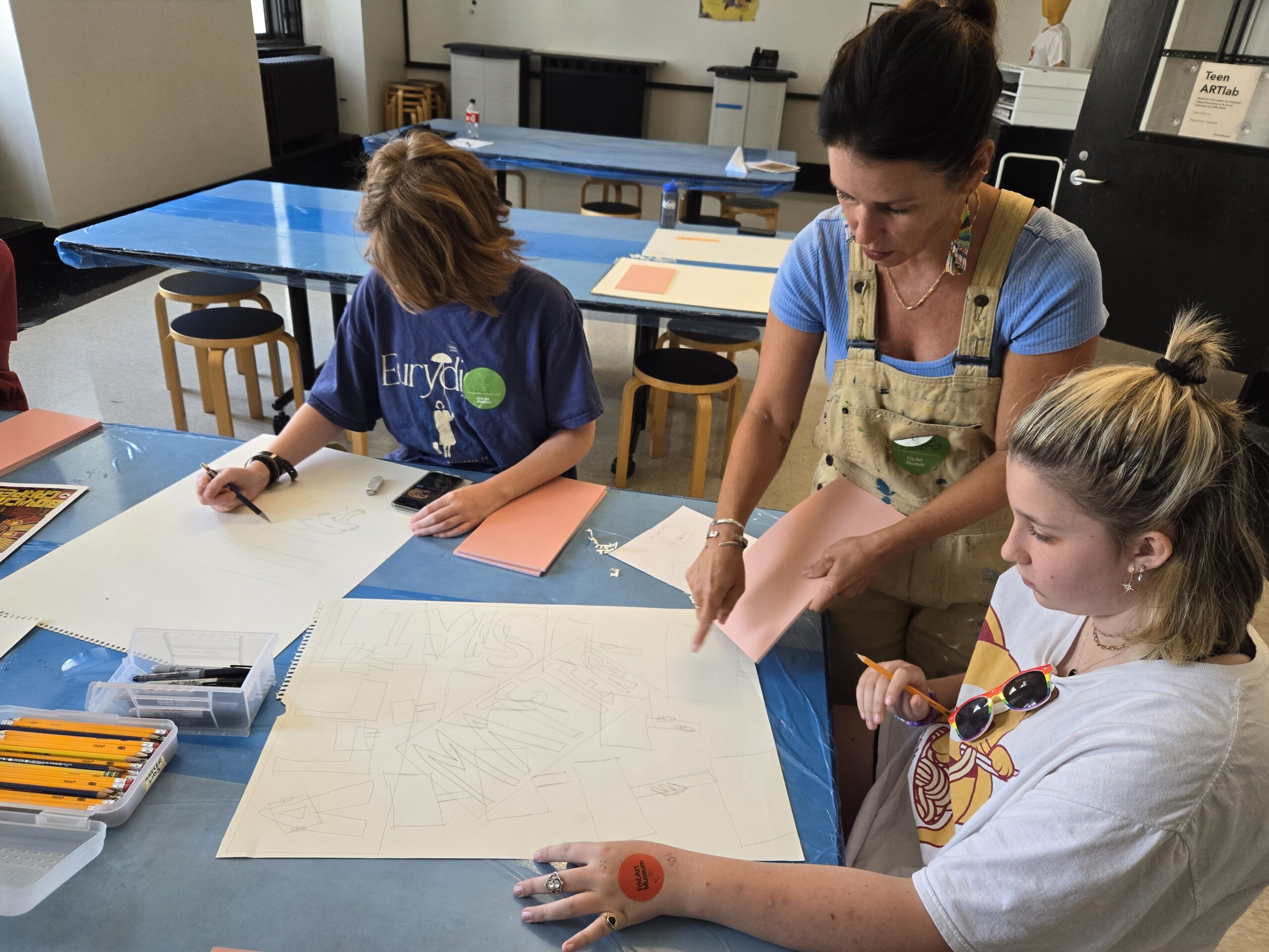 Three people work on drawings in an art class.