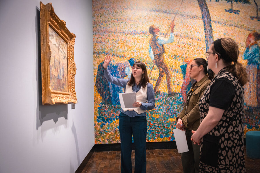 A woman gives a tour to others in an art gallery with impressionism works.