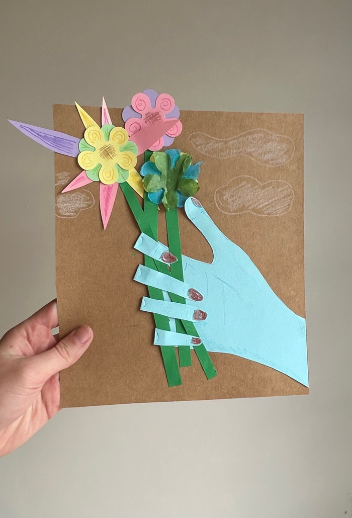 An art piece of a paper hand holding a bouquet of paper flowers. 