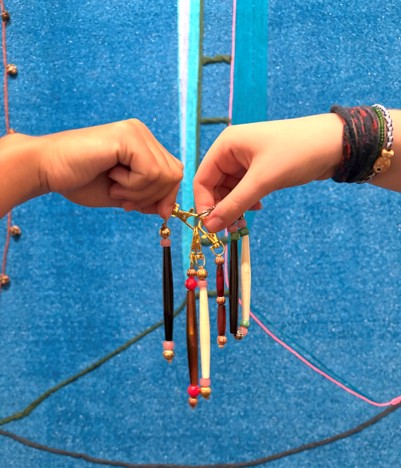 Two hands hold up a handmade keychain in front of an artwork.