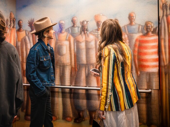 Two women inside an elevator looking at artwork on the walls