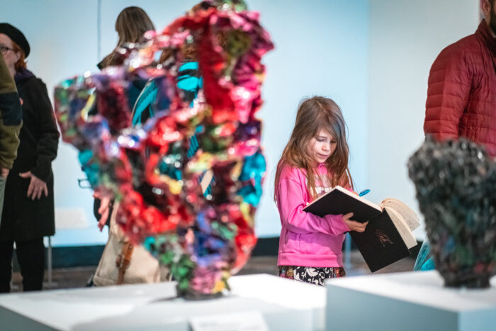 A young girl draws in a journal in an art gallery.
