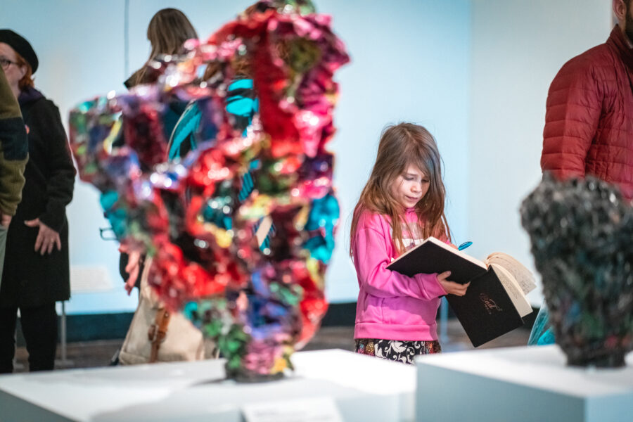 A young girl draws in a journal in an art gallery.